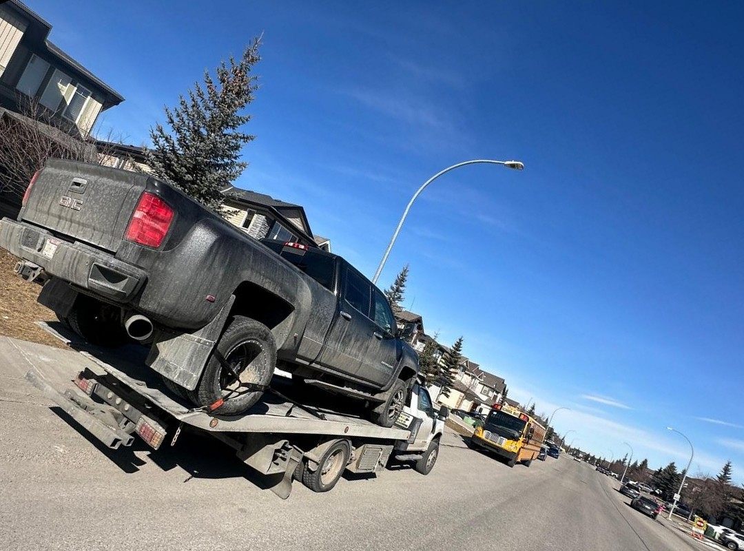 AR Towing flatbed truck hauling a pickup down a residential Calgary street