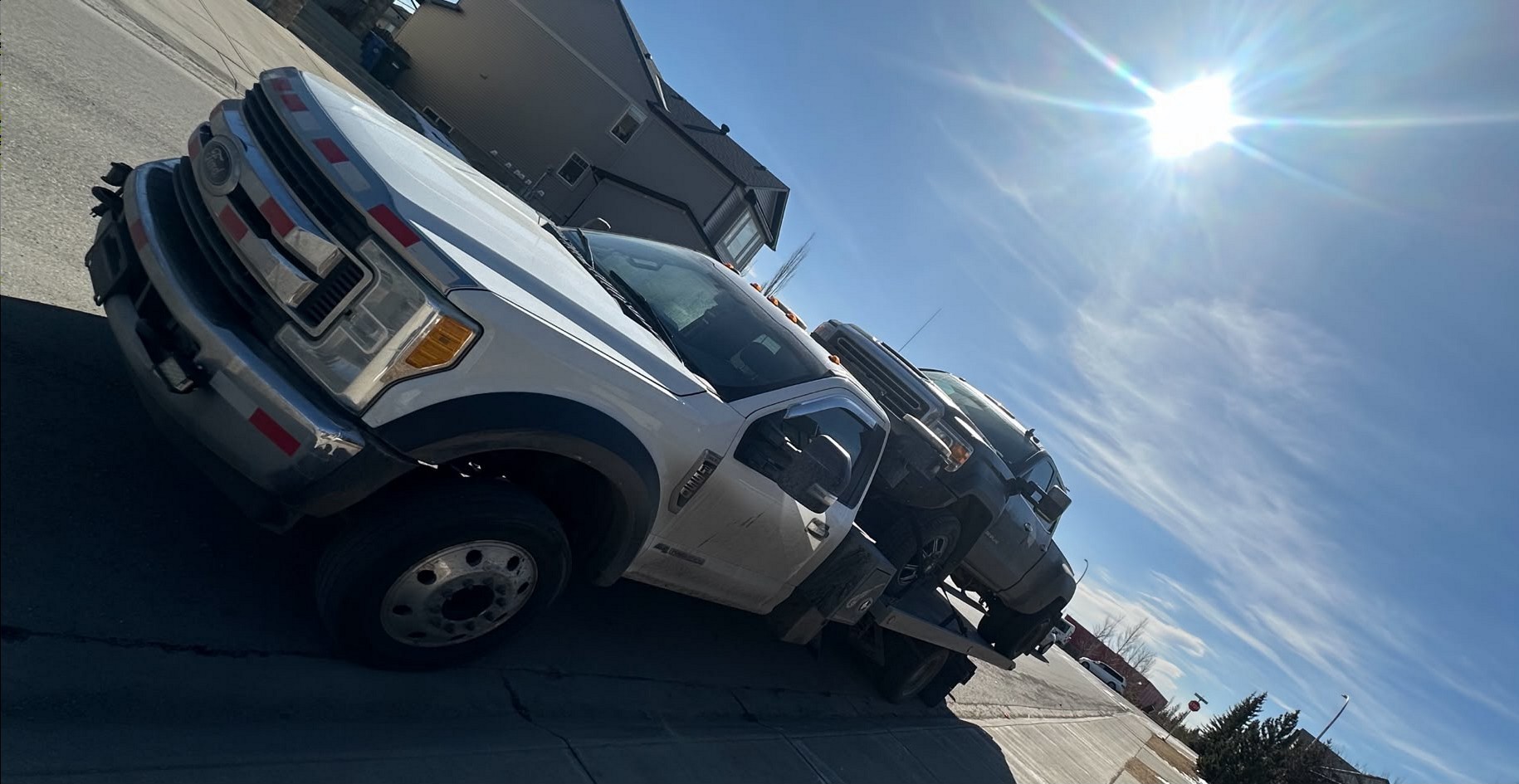 AR Towing flatbed truck hauling two pickups down a sunlit Calgary street