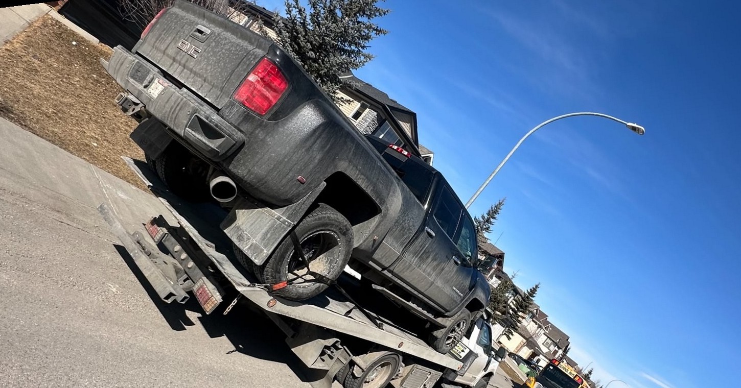 AR Towing flatbed truck hauling a pickup past a Calgary school bus